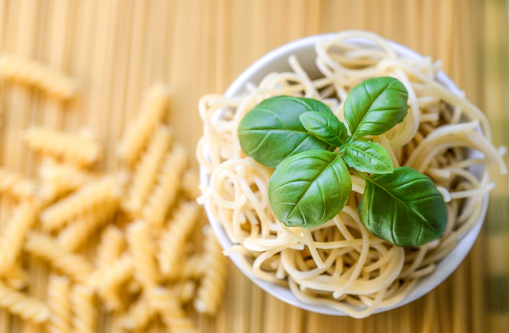 A bowl of fresh spaghetti garnished with basil leaves, perfect for a healthy Italian meal.